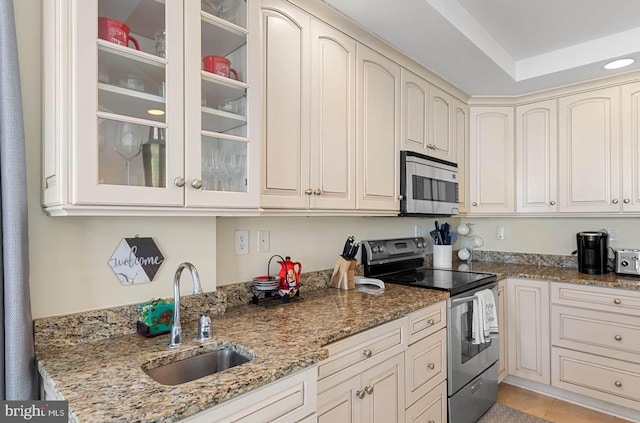 kitchen with sink, light tile patterned floors, stainless steel appliances, light stone counters, and a tray ceiling