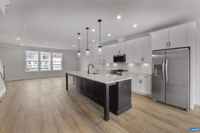 kitchen with appliances with stainless steel finishes, decorative light fixtures, white cabinetry, sink, and a kitchen island with sink