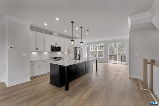 kitchen with appliances with stainless steel finishes, ornamental molding, an island with sink, white cabinets, and decorative light fixtures