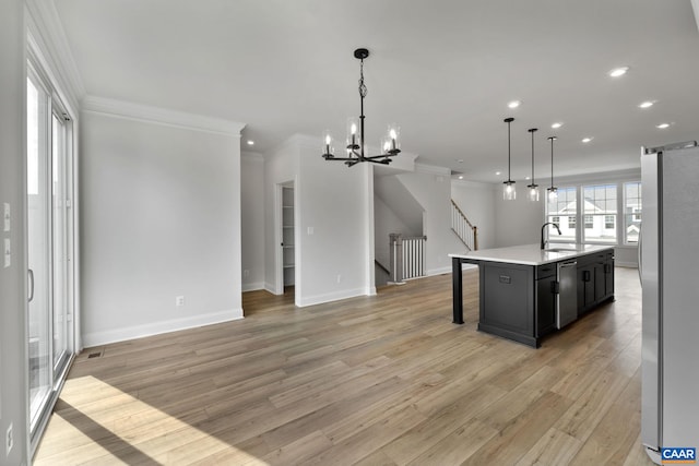 kitchen with appliances with stainless steel finishes, sink, hanging light fixtures, a kitchen island with sink, and light hardwood / wood-style floors