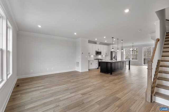 unfurnished living room featuring crown molding, a notable chandelier, sink, and light wood-type flooring