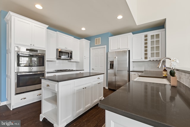 kitchen with visible vents, dark countertops, appliances with stainless steel finishes, a center island, and a sink