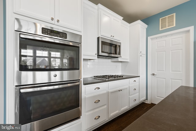 kitchen featuring visible vents, white cabinetry, appliances with stainless steel finishes, decorative backsplash, and dark countertops