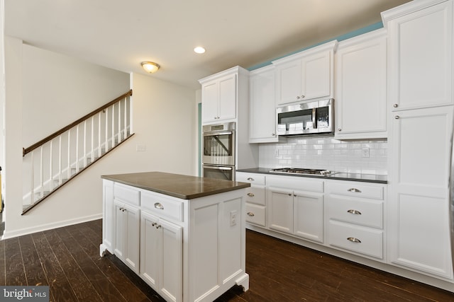 kitchen featuring dark countertops, dark wood-style floors, stainless steel appliances, white cabinetry, and backsplash