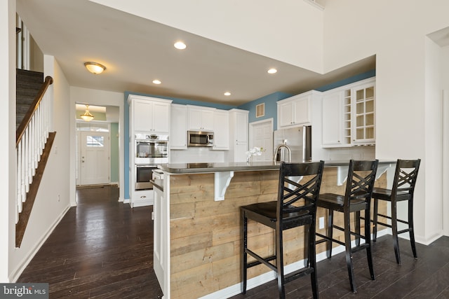 kitchen featuring stainless steel appliances, backsplash, a kitchen bar, and dark wood-style floors