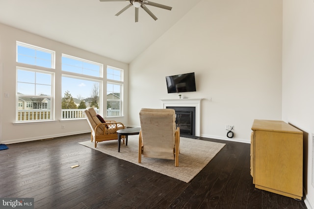 living area featuring high vaulted ceiling, dark wood-type flooring, a fireplace with flush hearth, a ceiling fan, and baseboards