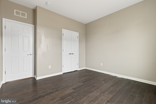 unfurnished bedroom featuring dark wood-style floors, a closet, visible vents, and baseboards