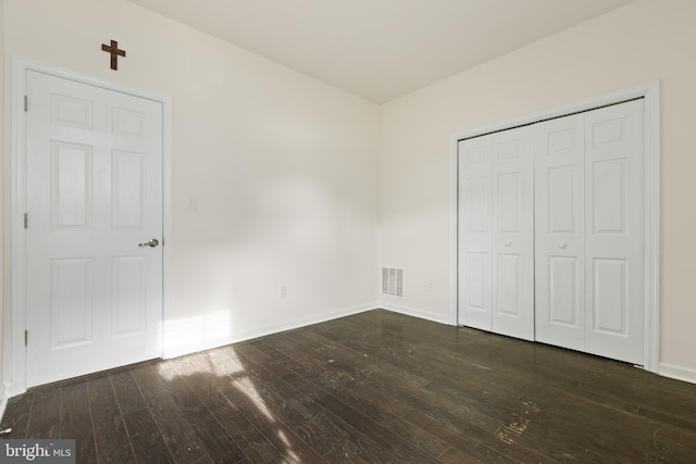 unfurnished bedroom with a closet, dark wood-style flooring, visible vents, and baseboards