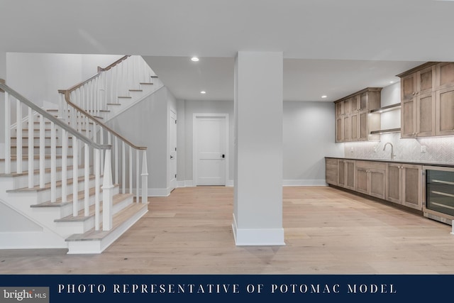 interior space featuring tasteful backsplash, light wood-type flooring, baseboards, wine cooler, and a sink