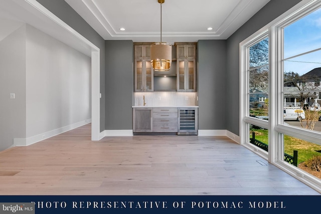 unfurnished dining area featuring a bar, baseboards, light wood-type flooring, and wine cooler