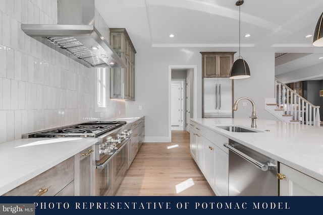 kitchen featuring a tray ceiling, decorative backsplash, a sink, high quality appliances, and wall chimney exhaust hood