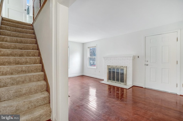 unfurnished living room with a brick fireplace and dark wood-type flooring