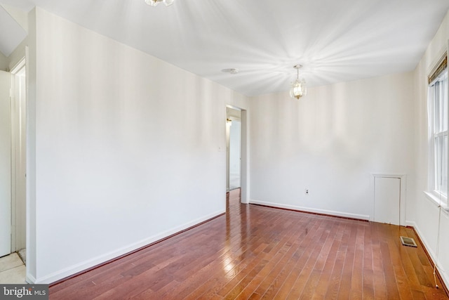 empty room with hardwood / wood-style floors and an inviting chandelier