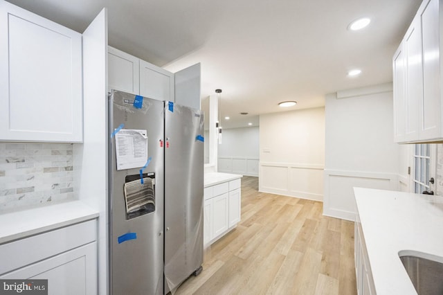 kitchen with white cabinetry, light wood-type flooring, stainless steel refrigerator, pendant lighting, and backsplash