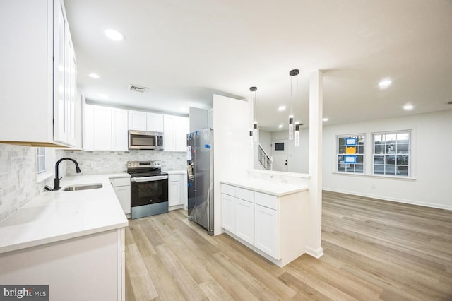 kitchen featuring appliances with stainless steel finishes, pendant lighting, white cabinetry, sink, and light wood-type flooring