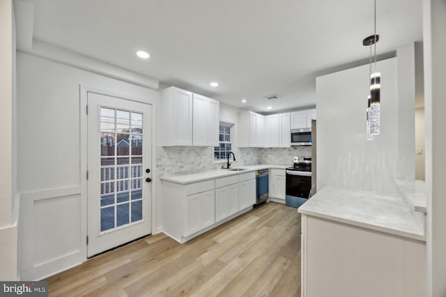 kitchen with appliances with stainless steel finishes, hanging light fixtures, light hardwood / wood-style floors, white cabinets, and decorative backsplash