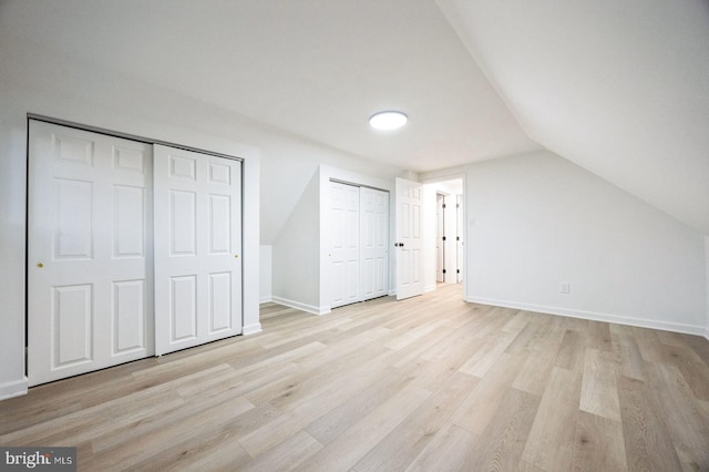 unfurnished bedroom with vaulted ceiling, light wood-type flooring, and two closets