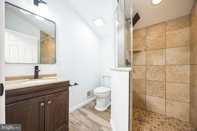 bathroom with hardwood / wood-style flooring, tiled shower, vanity, and toilet