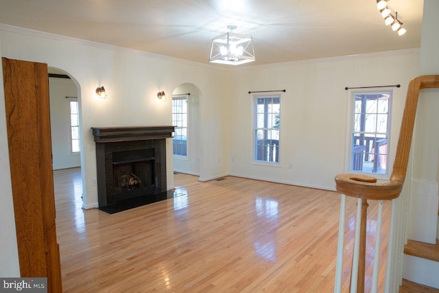 unfurnished living room featuring crown molding, an inviting chandelier, and light wood-type flooring