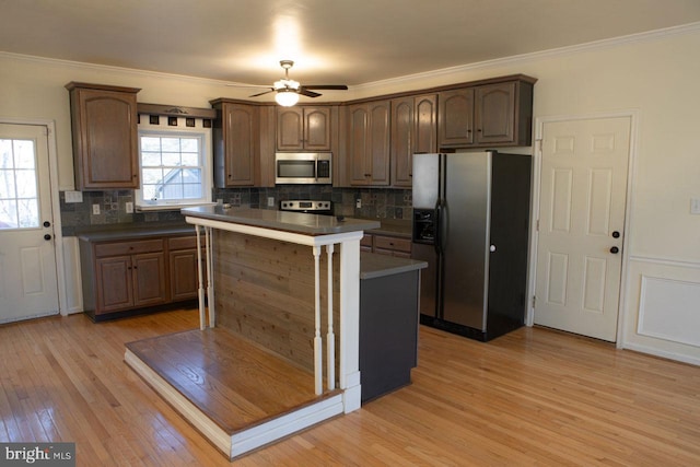 kitchen with crown molding, a kitchen island, stainless steel appliances, light hardwood / wood-style floors, and decorative backsplash