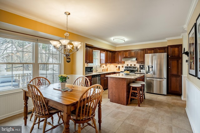 dining room with an inviting chandelier, a decorative wall, crown molding, and wainscoting