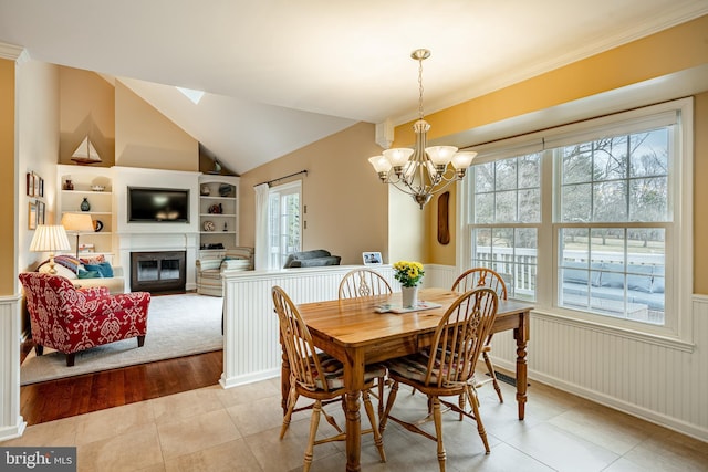 tiled dining area featuring built in shelves, a glass covered fireplace, wainscoting, lofted ceiling, and a chandelier