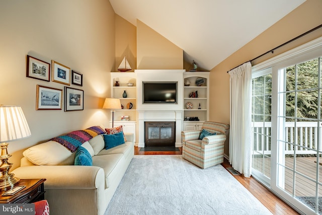 living area with a fireplace with flush hearth, wood finished floors, and high vaulted ceiling