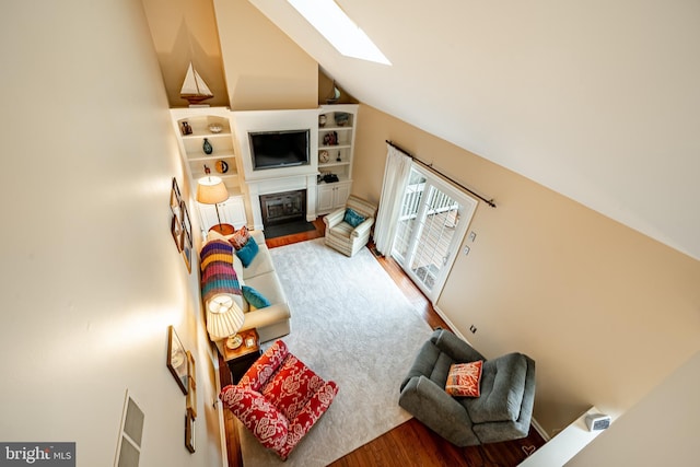 living area with lofted ceiling with skylight, a fireplace, and wood finished floors