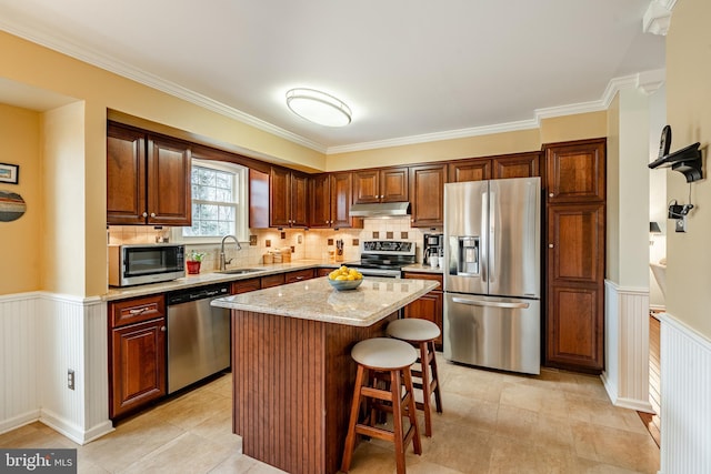 kitchen featuring under cabinet range hood, a wainscoted wall, appliances with stainless steel finishes, and a sink