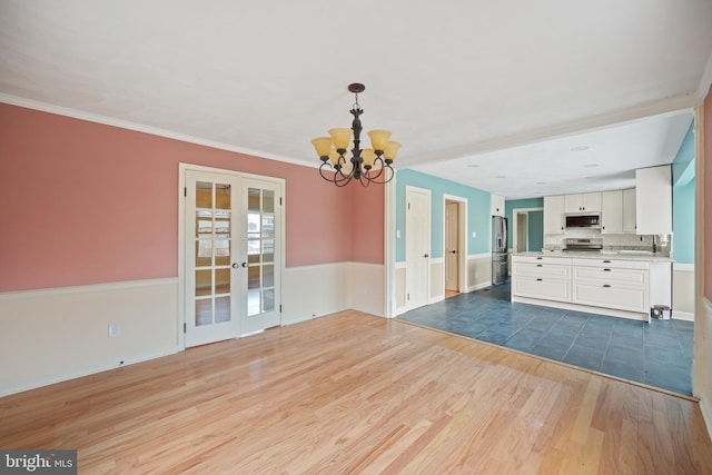 unfurnished living room with sink, dark wood-type flooring, ornamental molding, french doors, and a chandelier