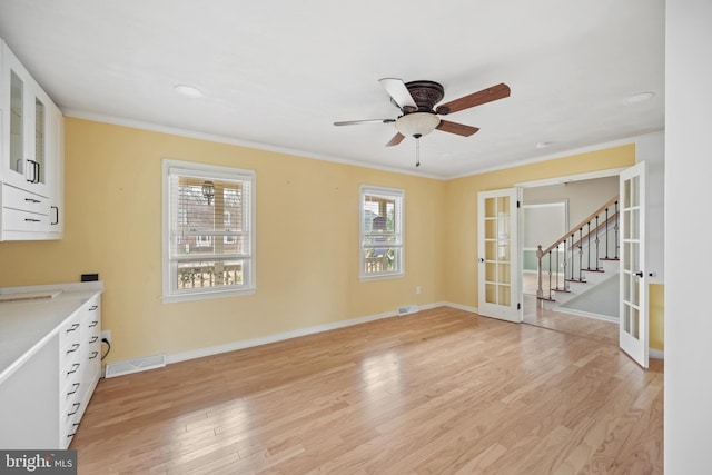 unfurnished living room with crown molding, light hardwood / wood-style flooring, french doors, and ceiling fan