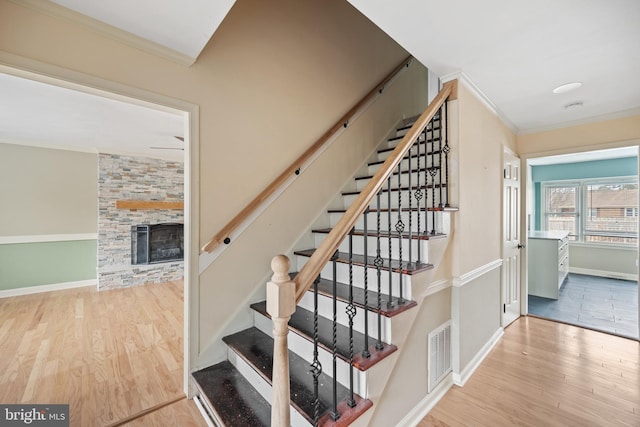 stairway with ornamental molding, a stone fireplace, and hardwood / wood-style floors