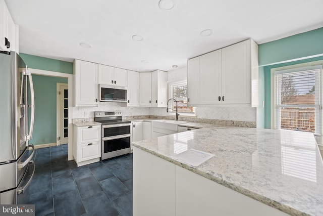 kitchen with light stone counters, stainless steel appliances, tasteful backsplash, and white cabinets