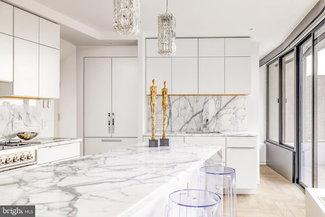 kitchen featuring sink, white cabinetry, tasteful backsplash, decorative light fixtures, and light parquet flooring