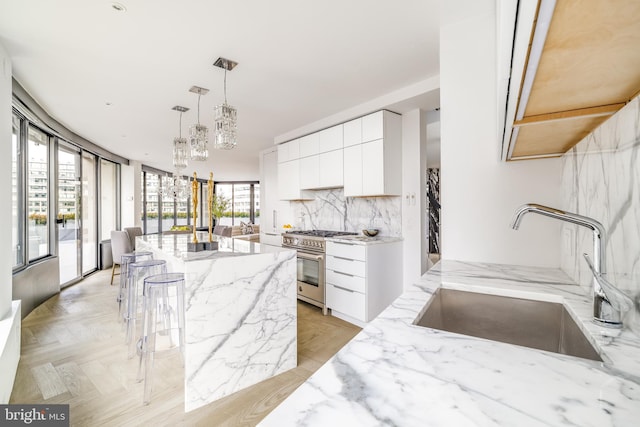 kitchen with decorative light fixtures, white cabinetry, sink, a center island, and high end stainless steel range