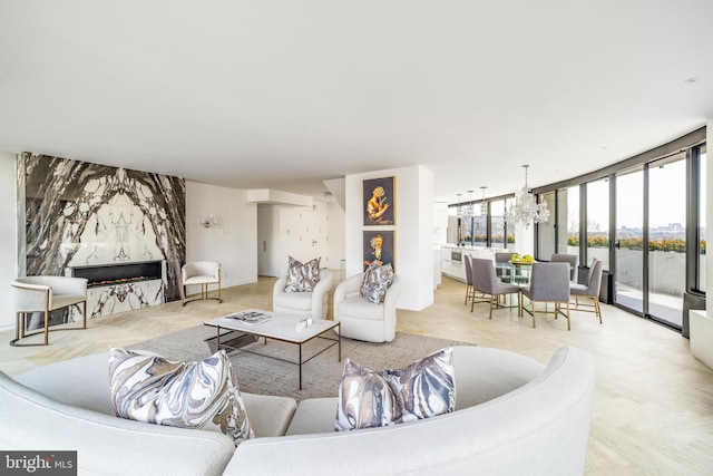 living room featuring light parquet floors, a premium fireplace, a notable chandelier, and a wall of windows