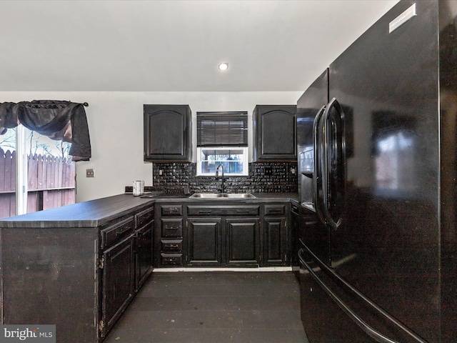 kitchen featuring dark countertops, black fridge with ice dispenser, decorative backsplash, a sink, and a peninsula