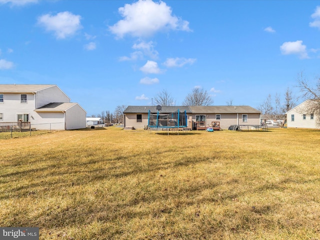 rear view of property featuring a trampoline and a lawn