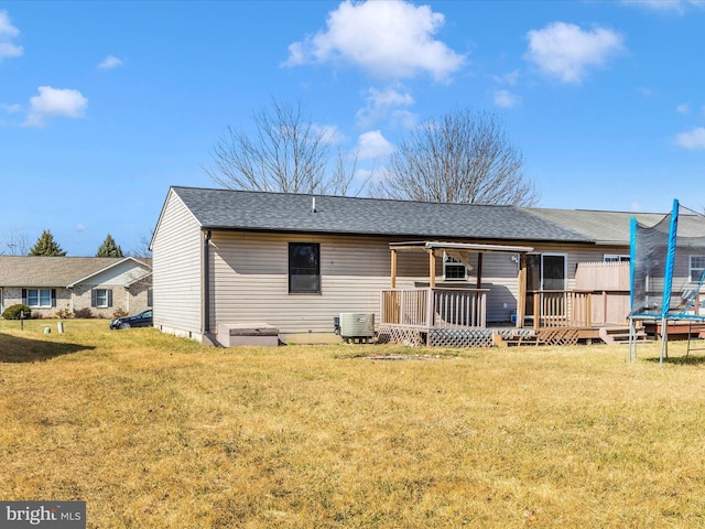 rear view of house featuring a trampoline, central AC, a yard, and a shingled roof