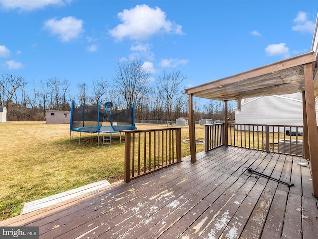 deck featuring an outbuilding, a storage unit, a trampoline, and a lawn