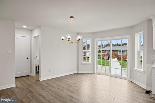 unfurnished dining area featuring an inviting chandelier and light hardwood / wood-style flooring