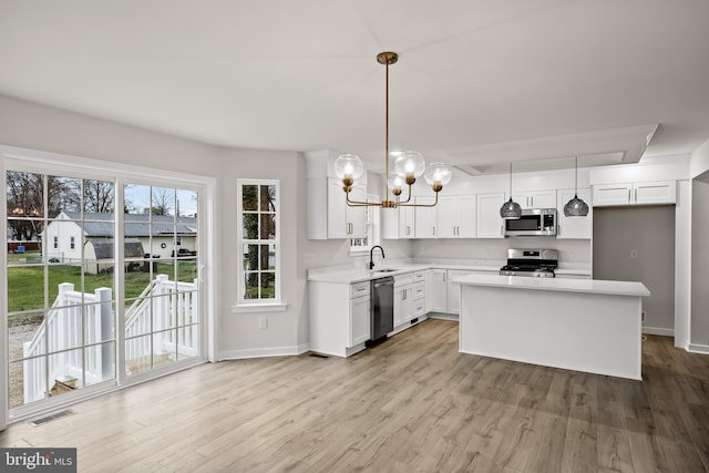 kitchen with sink, white cabinetry, appliances with stainless steel finishes, pendant lighting, and light hardwood / wood-style floors