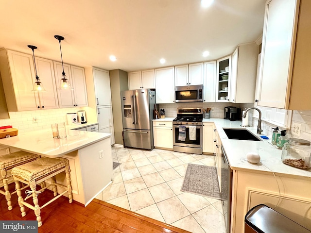 kitchen with appliances with stainless steel finishes, pendant lighting, white cabinetry, sink, and a breakfast bar area