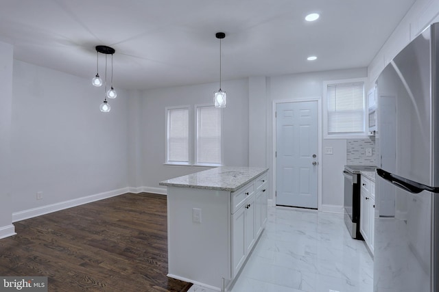 kitchen with appliances with stainless steel finishes, white cabinetry, light stone countertops, a kitchen island, and decorative light fixtures