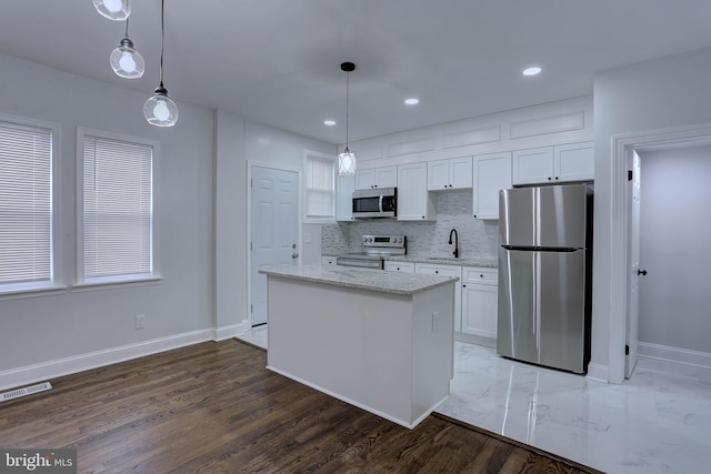 kitchen with pendant lighting, white cabinetry, a center island, light stone counters, and stainless steel appliances