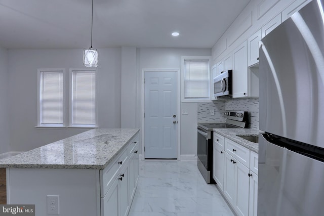 kitchen featuring appliances with stainless steel finishes, white cabinetry, a center island, light stone countertops, and decorative light fixtures