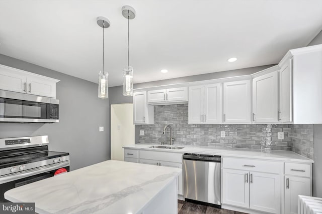 kitchen with appliances with stainless steel finishes, pendant lighting, tasteful backsplash, sink, and white cabinets