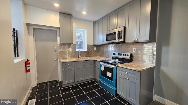 kitchen with gray cabinets, light stone countertops, appliances with stainless steel finishes, and sink