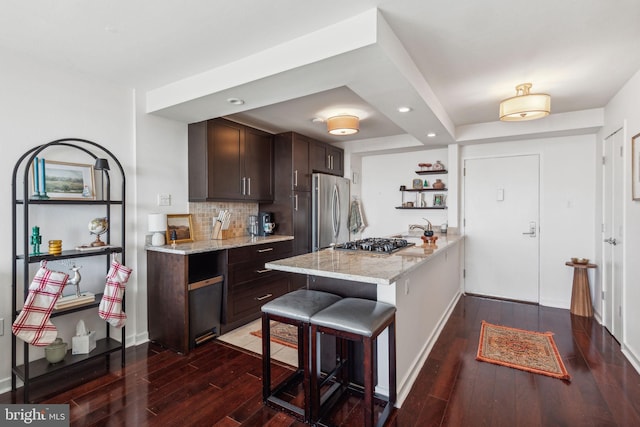 kitchen featuring stainless steel appliances, light stone counters, dark brown cabinetry, a kitchen bar, and kitchen peninsula