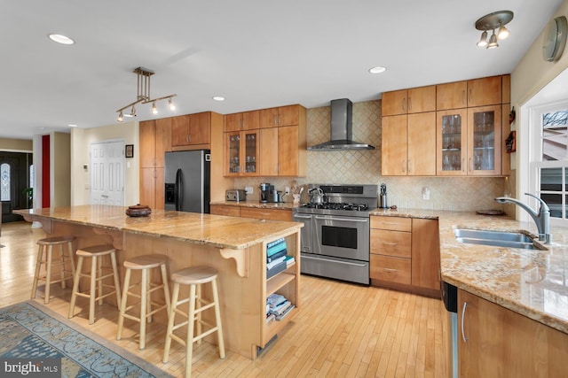 kitchen featuring wall chimney exhaust hood, a kitchen bar, sink, black fridge, and range with two ovens